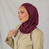 Woman wearing a burgundy ruched hijab and beige blazer against a plain background.