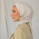 Woman wearing a beige ruching hijab and beige top against a plain background.