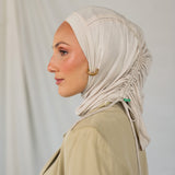 Woman wearing a beige ruching hijab and beige top against a plain background.