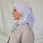 Woman wearing a lavender ruching hijab and beige suit against a plain background.
