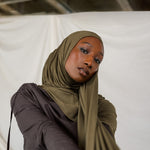 Woman wearing a green hijab and dark clothing against a white background