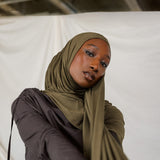 Woman wearing a green hijab and dark clothing against a white background