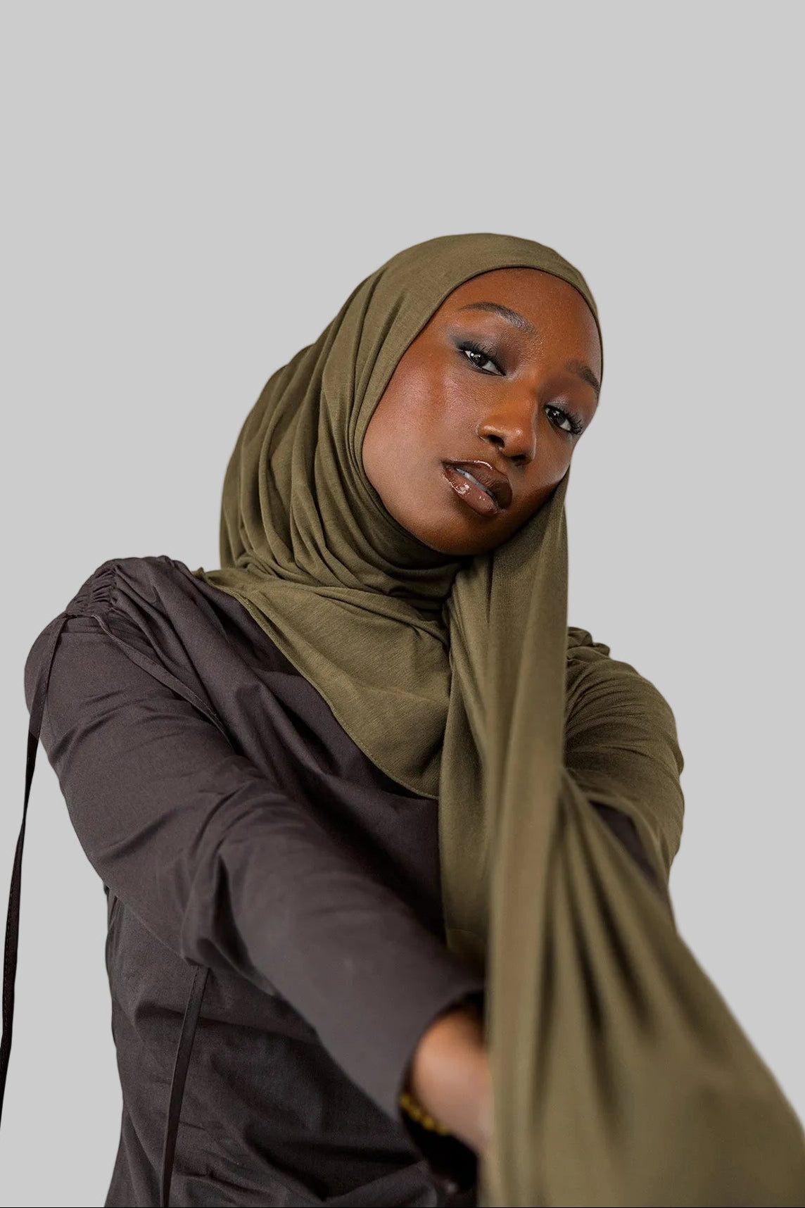 Woman wearing a green hijab and dark clothing against a white background