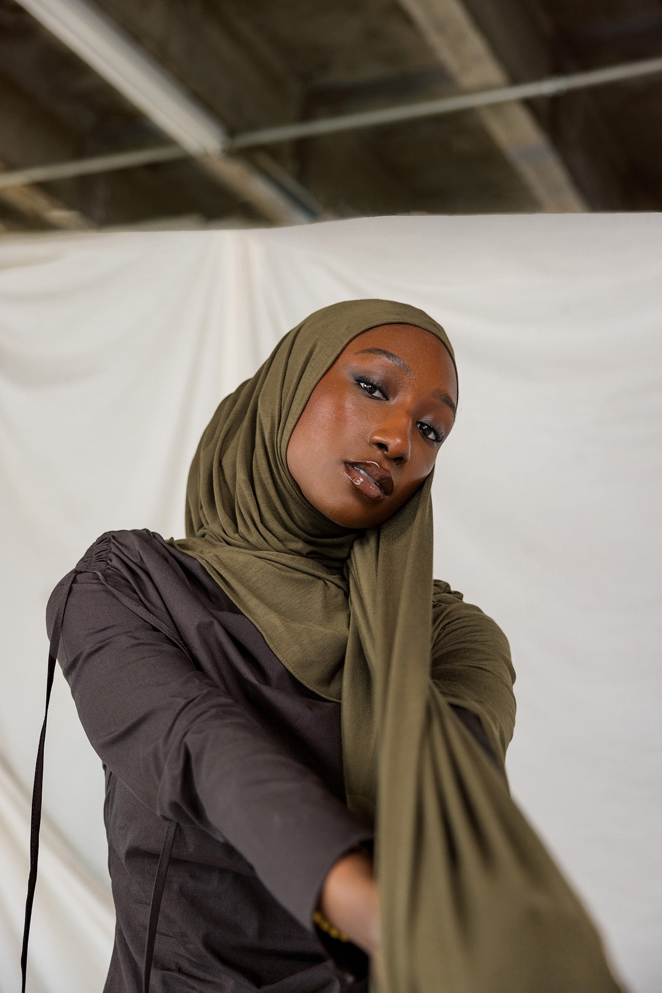 Woman wearing a green hijab and dark clothing against a white background