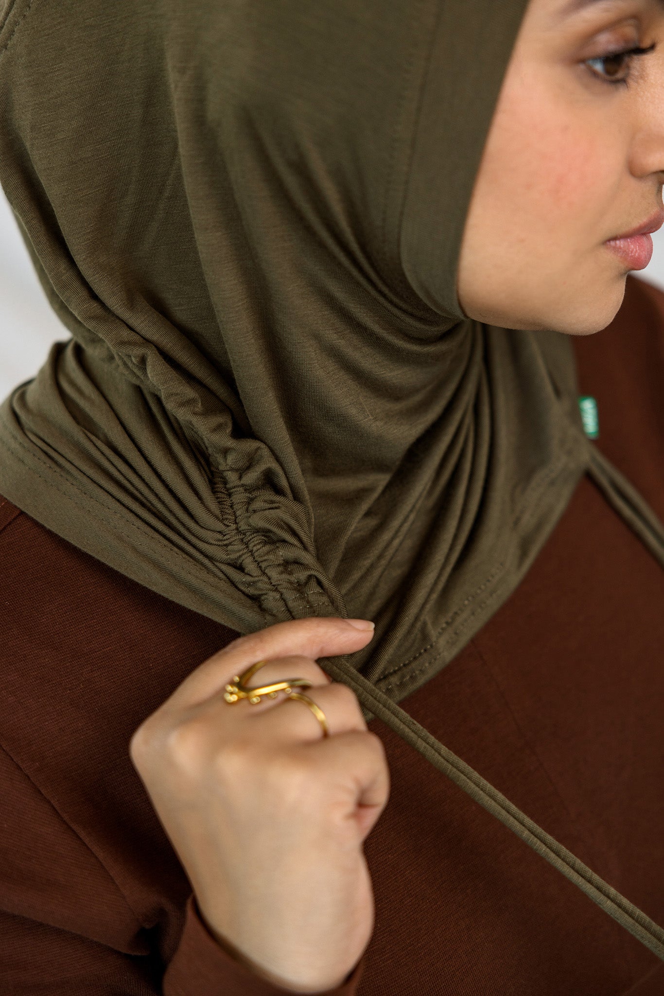 Woman wearing a green hijab adjusting it against a neutral background