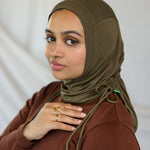 Woman wearing a brown hijab and brown top against a white background