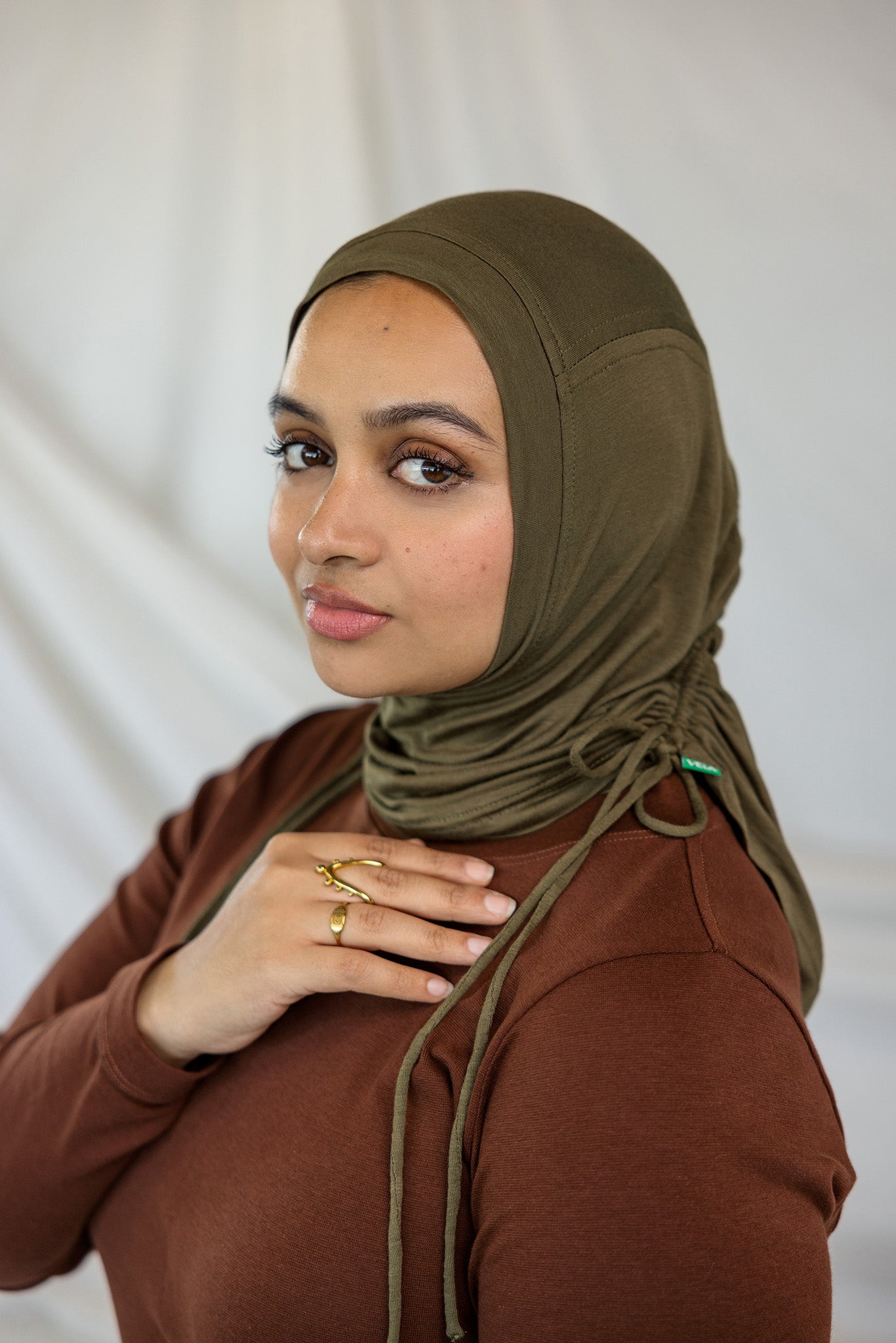 Woman wearing a brown hijab and brown top against a white background