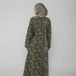 Woman wearing a green jacquard patterned abaya on a gray background