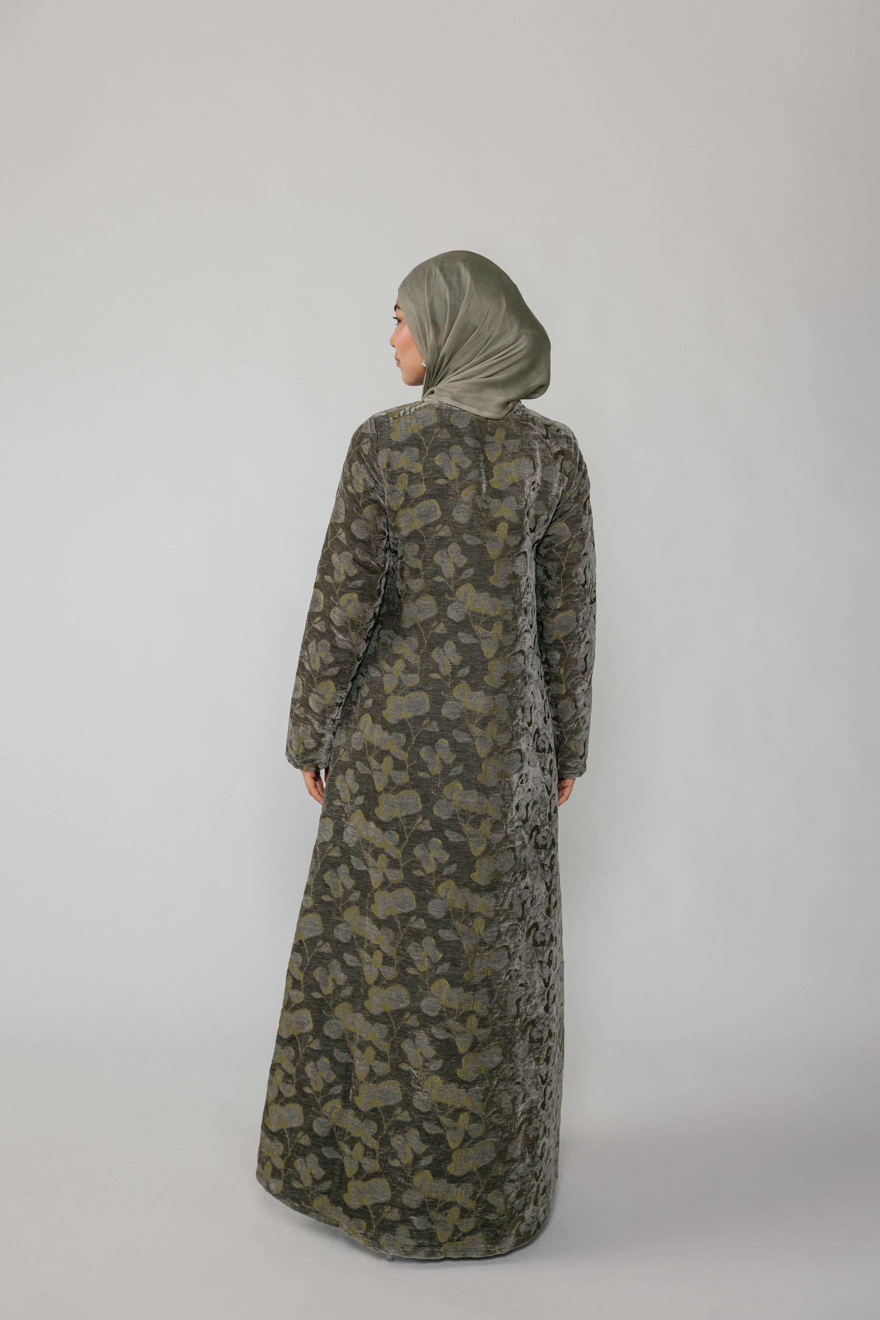 Woman wearing a green jacquard patterned abaya on a gray background