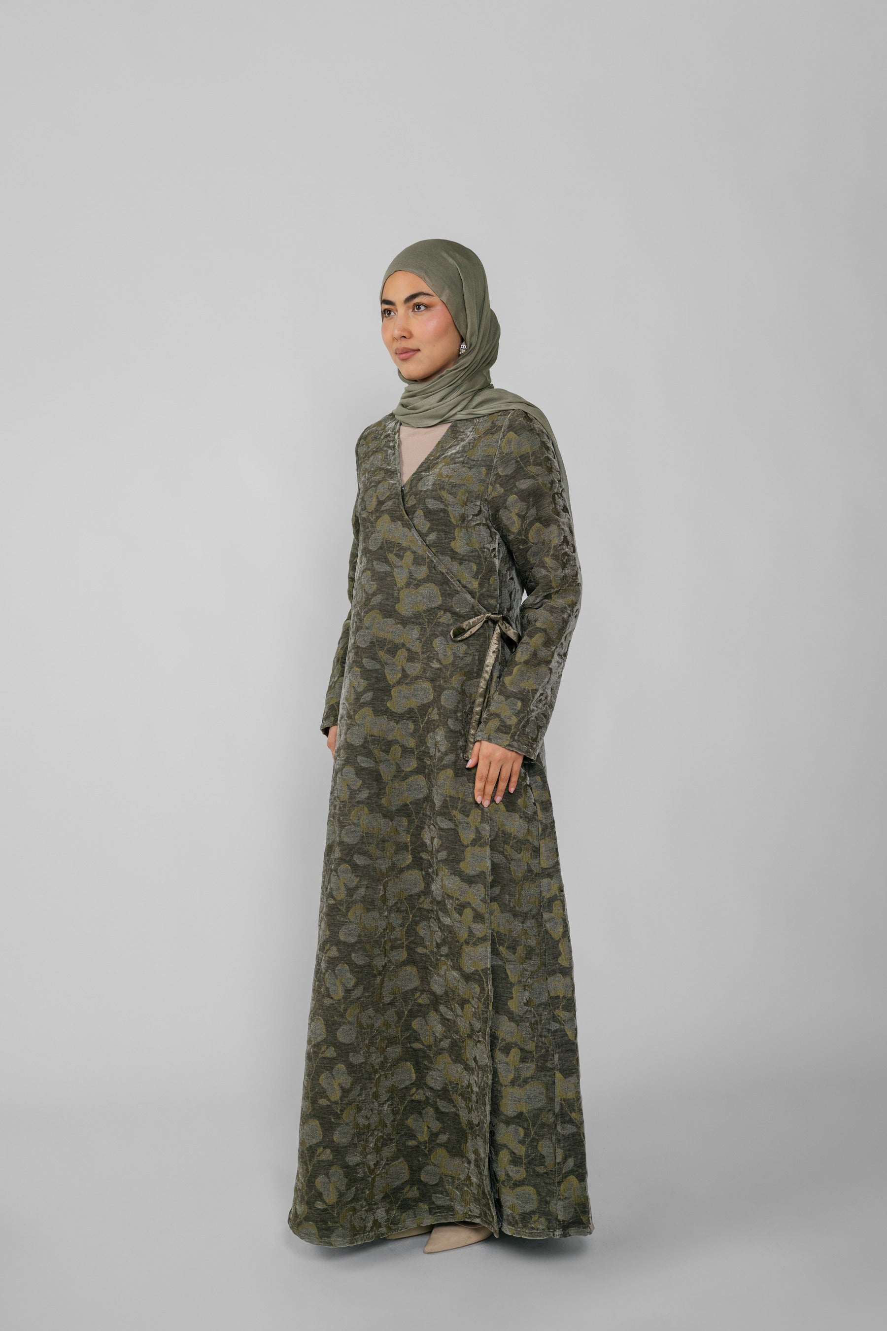 Woman wearing a green jacquard patterned abaya on a gray background