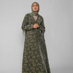 Woman wearing a green jacquard patterned abaya on a gray background