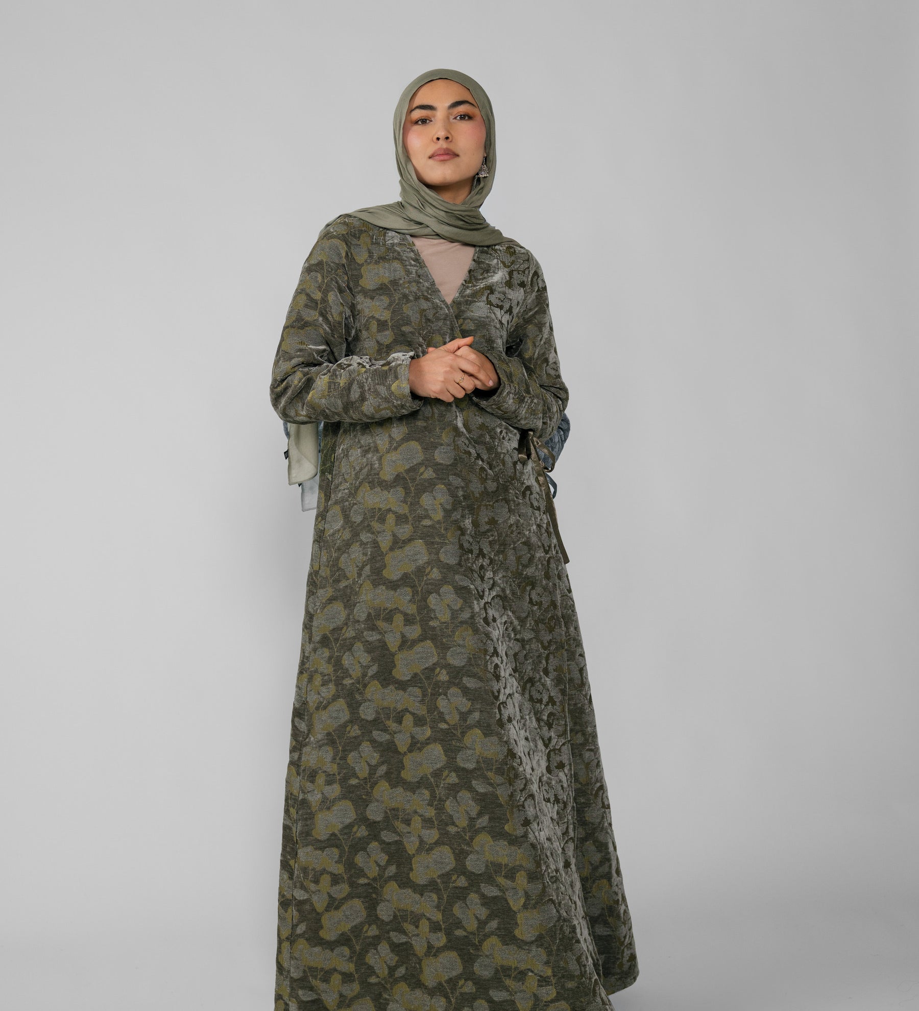 Woman wearing a green jacquard patterned abaya on a gray background