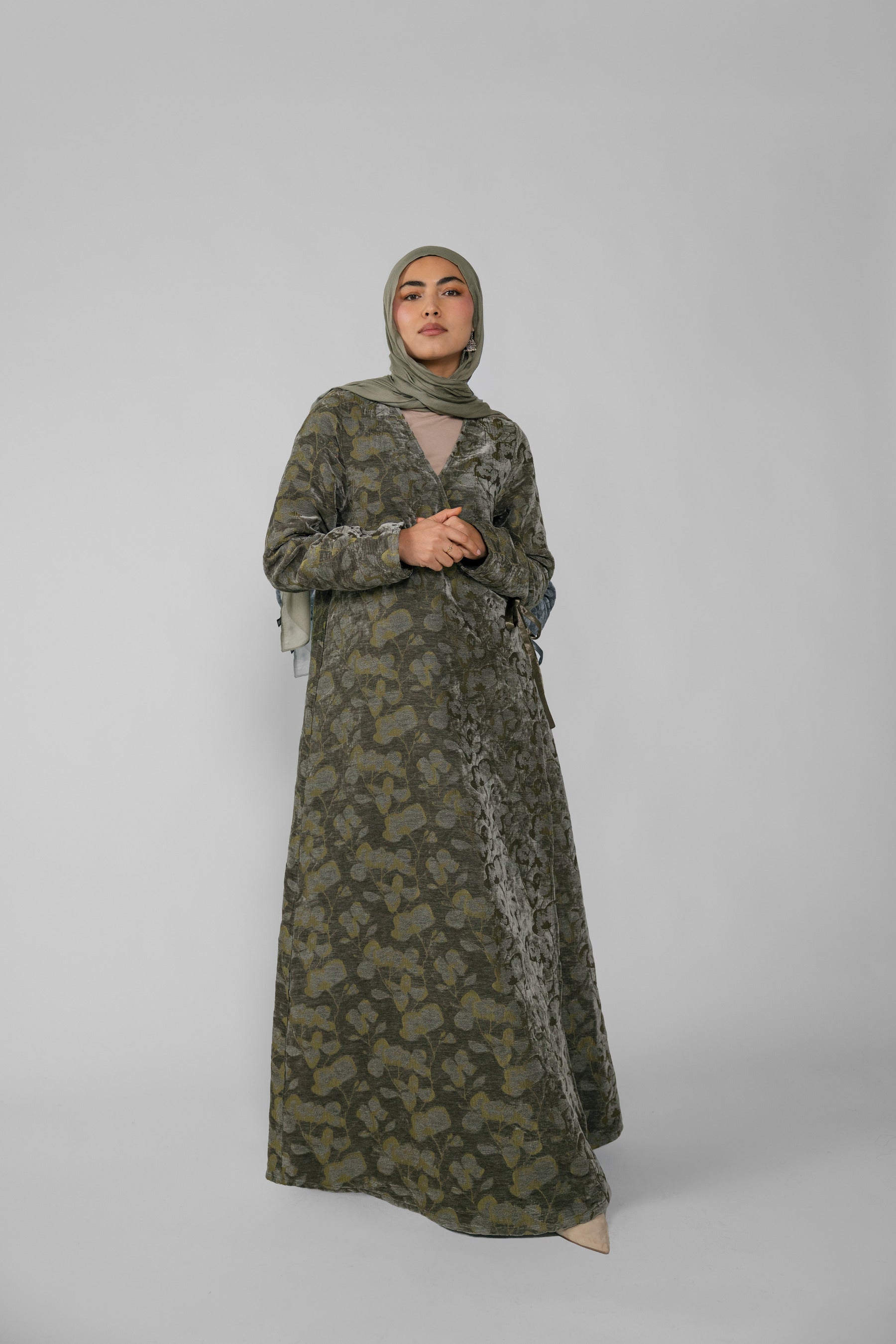 Woman wearing a green jacquard patterned abaya on a gray background