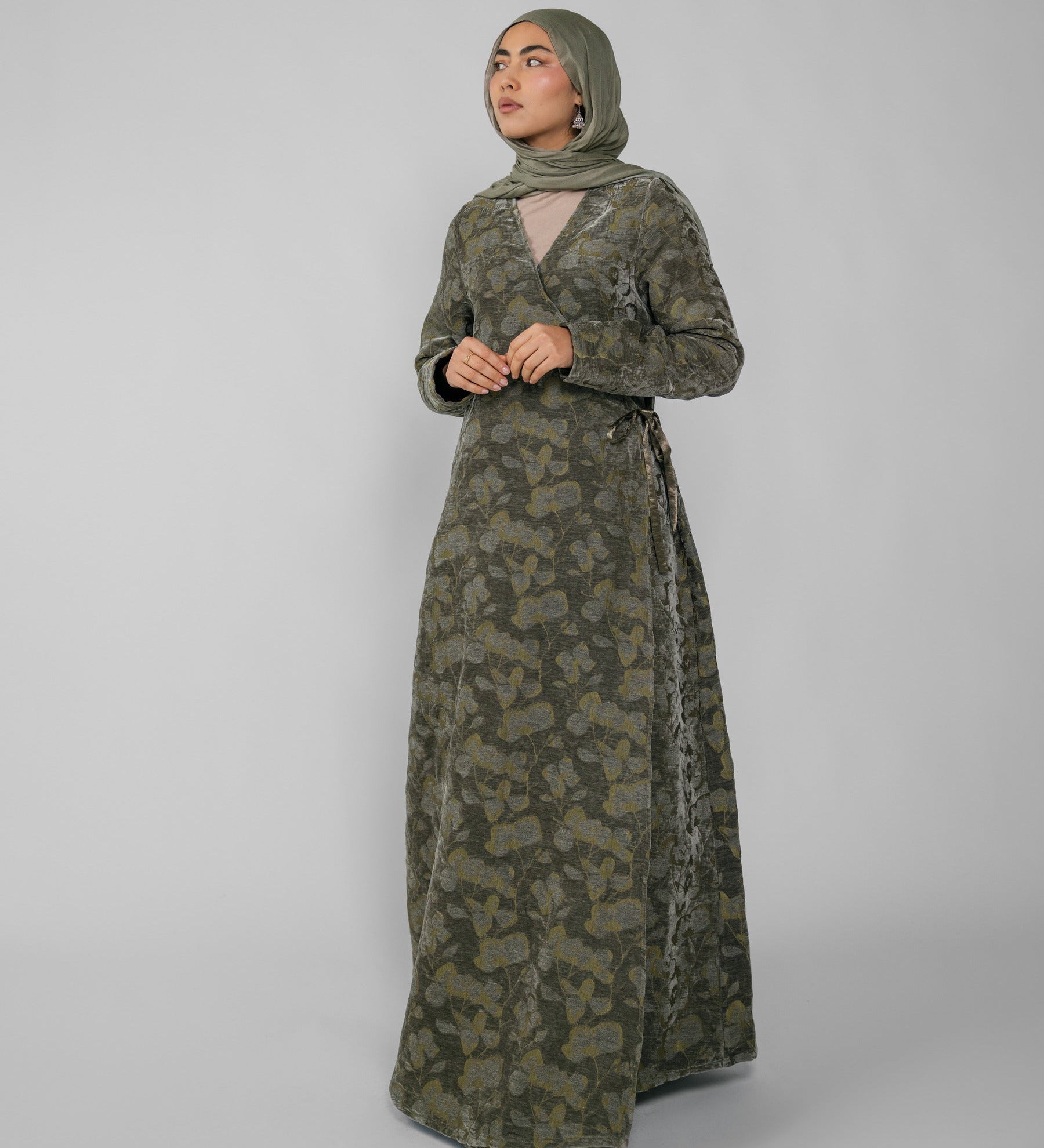 Woman wearing a green jacquard patterned abaya on a gray background