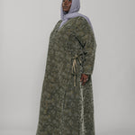 Woman wearing a green jacquard patterned abaya on a gray background