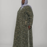 Woman wearing a green jacquard patterned abaya on a gray background