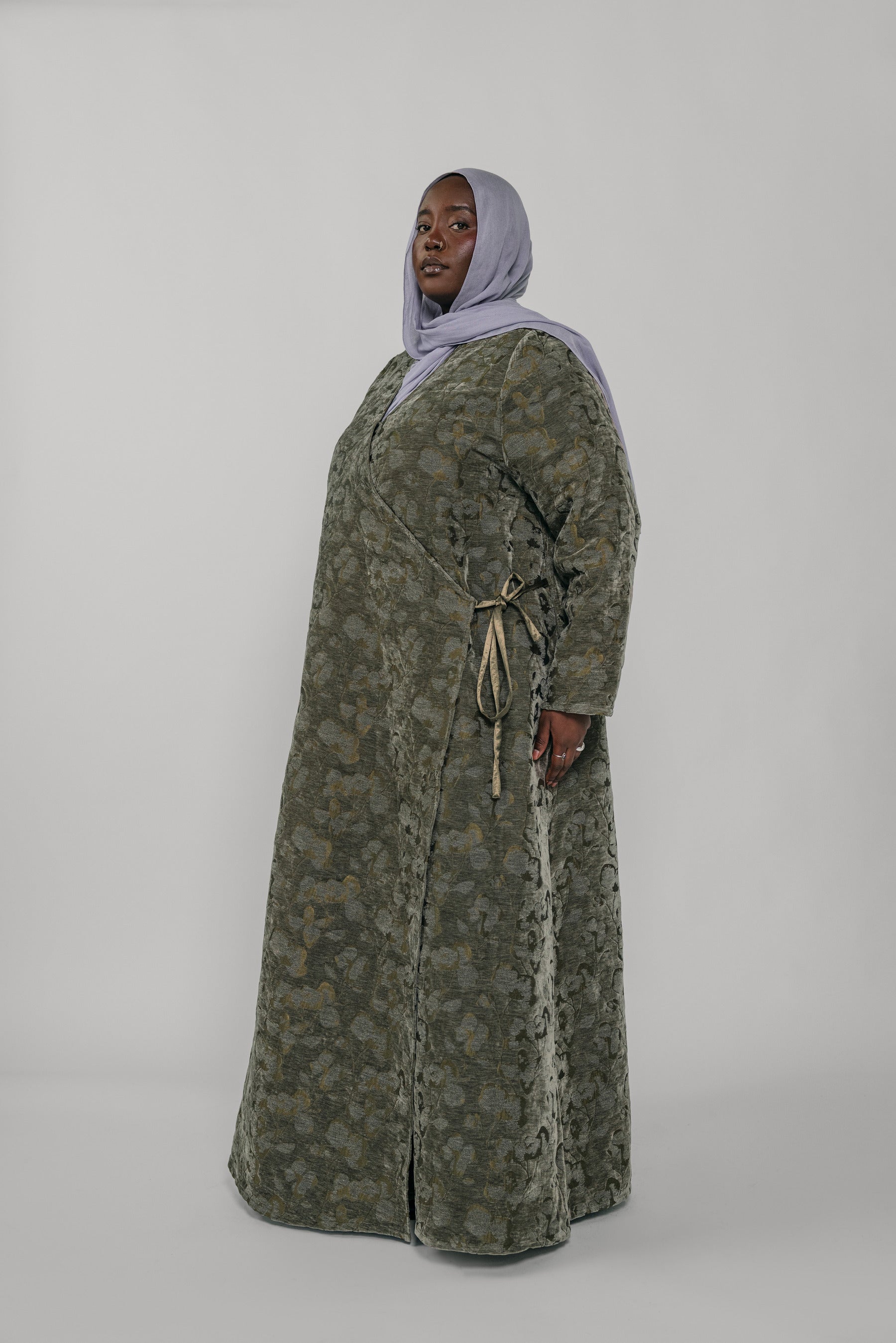 Woman wearing a green jacquard patterned abaya on a gray background