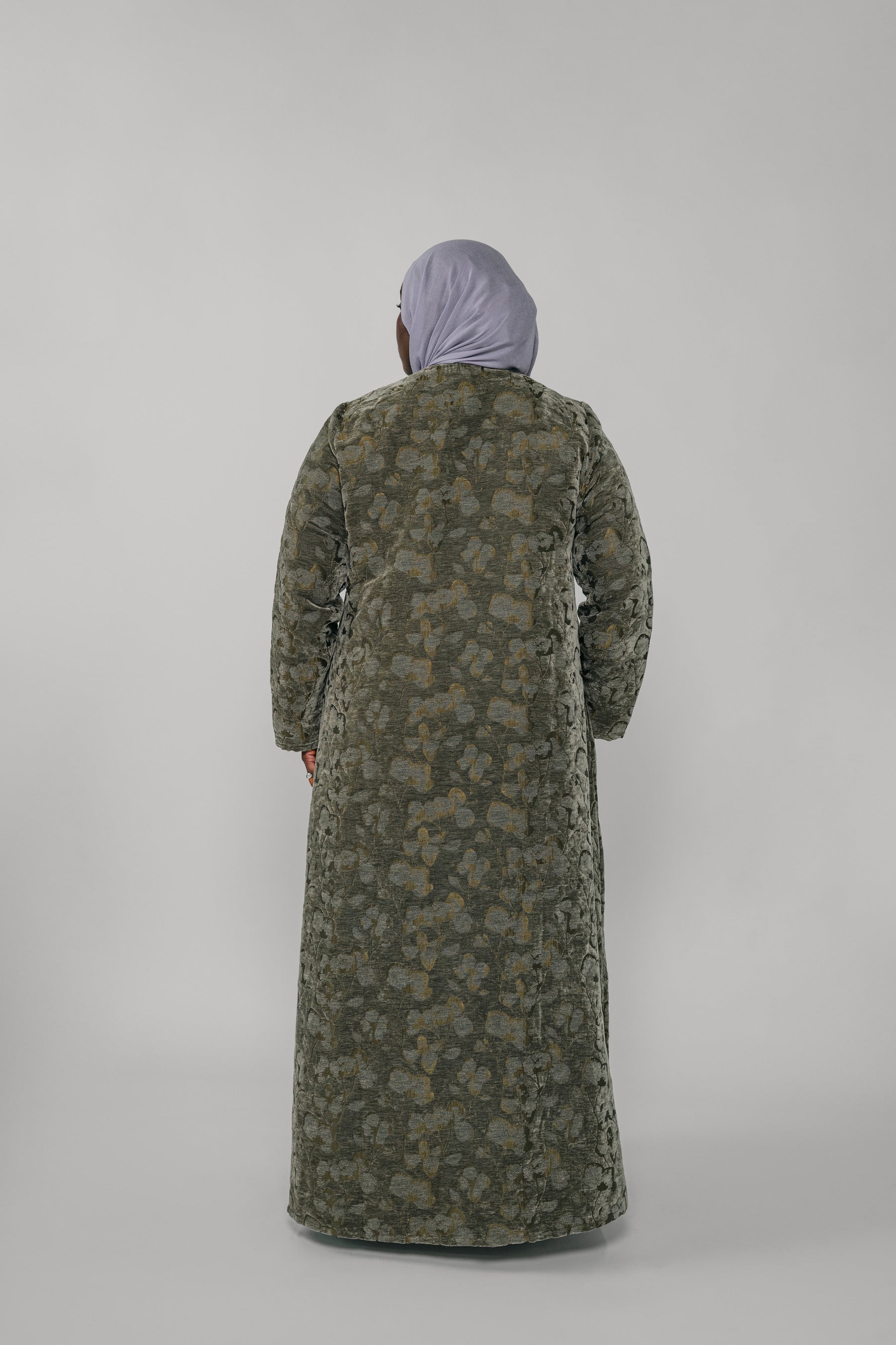 Woman wearing a green jacquard patterned abaya on a gray background