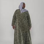 Woman wearing a green jacquard patterned abaya on a gray background