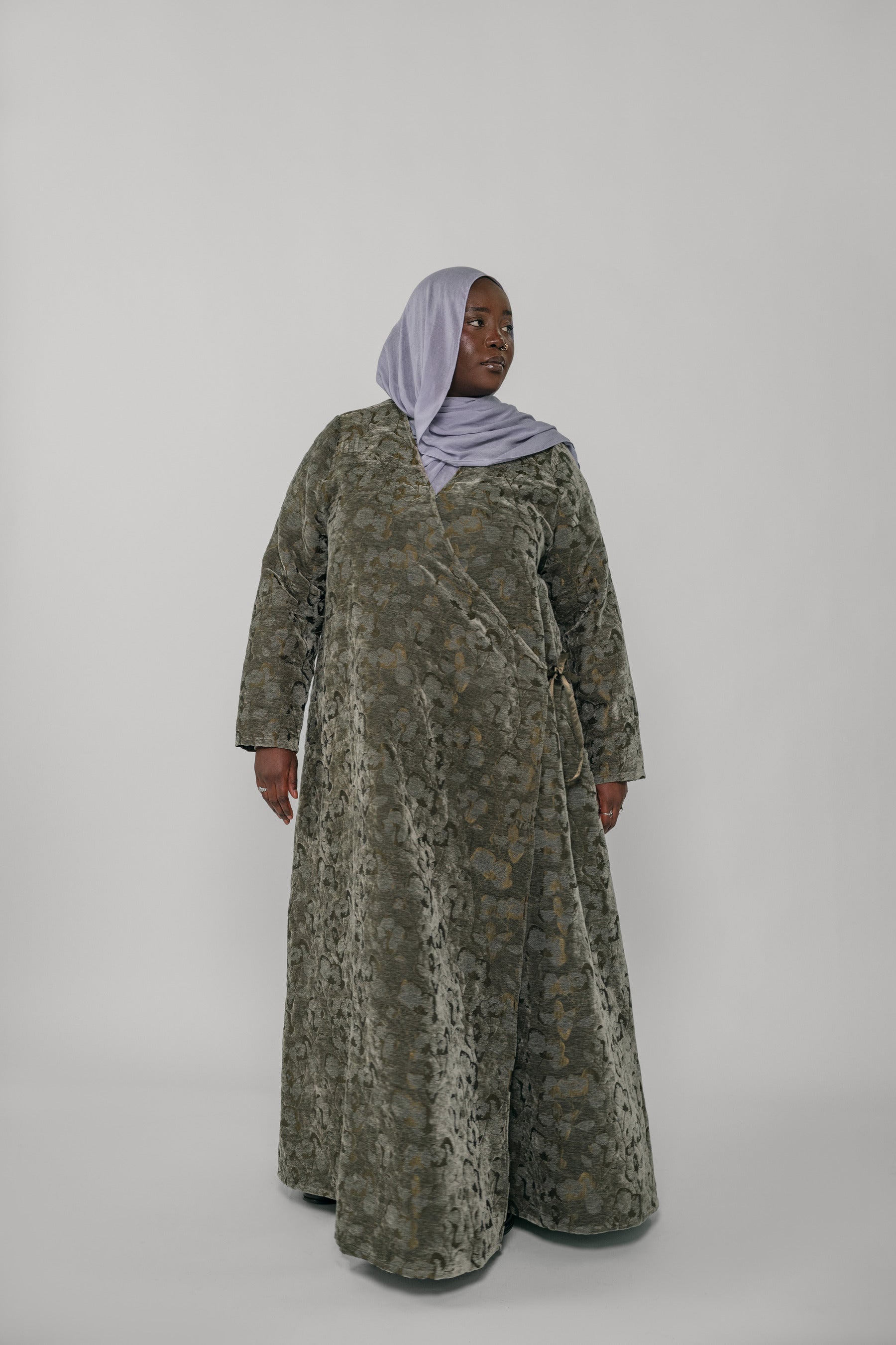 Woman wearing a green jacquard patterned abaya on a gray background