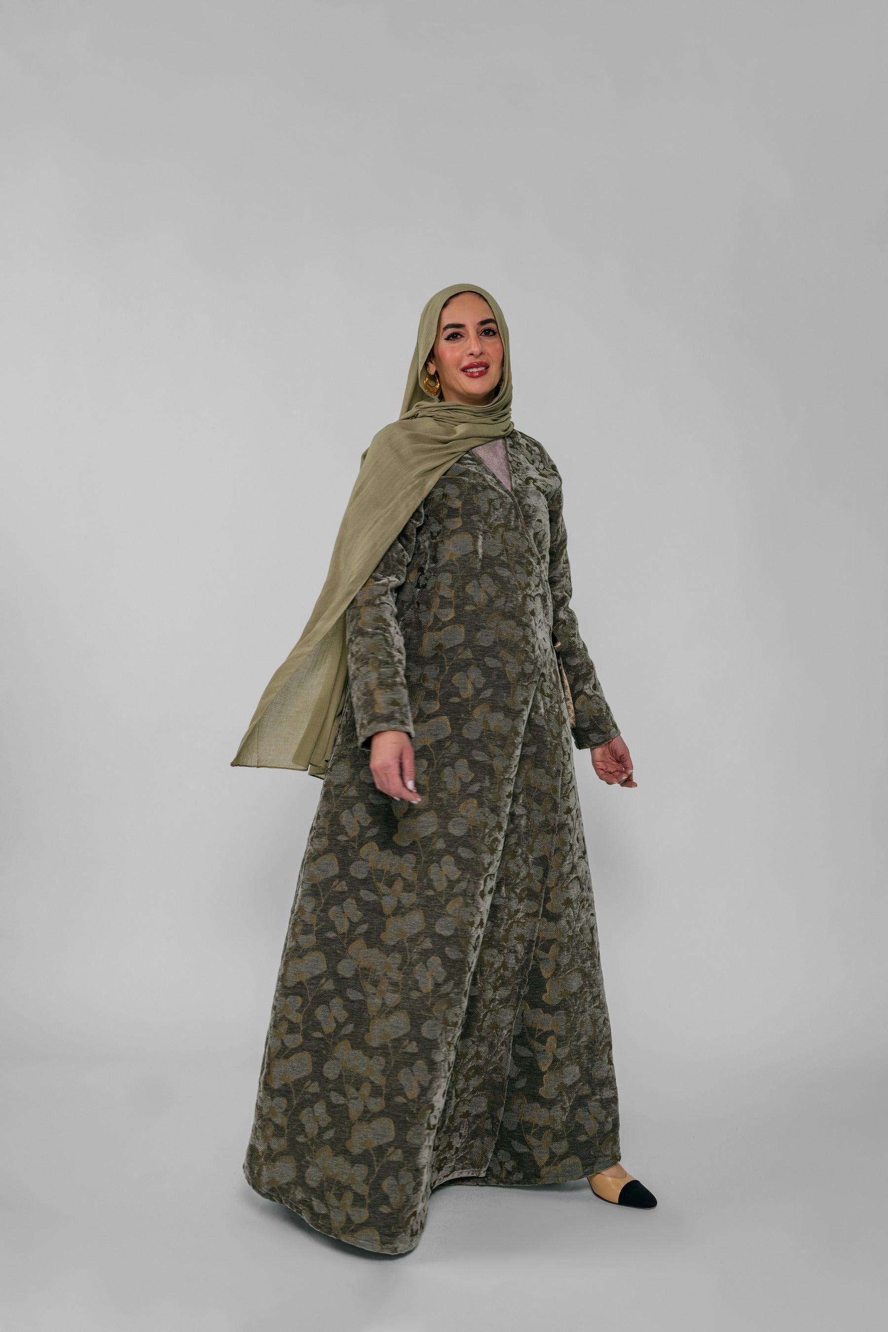 Woman wearing a green patterned abaya and matching hijab on a white background
