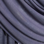 A close-up of draped fabric in a muted dusty purple showing the soft texture and folds against a light neutral background.