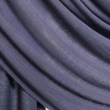 A close-up of draped fabric in a muted dusty purple showing the soft texture and folds against a light neutral background.