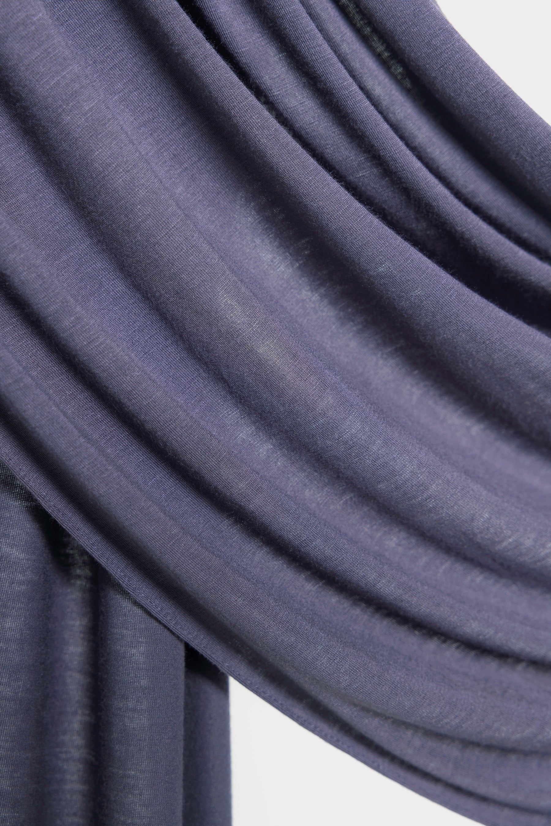A close-up of draped fabric in a muted dusty purple showing the soft texture and folds against a light neutral background.