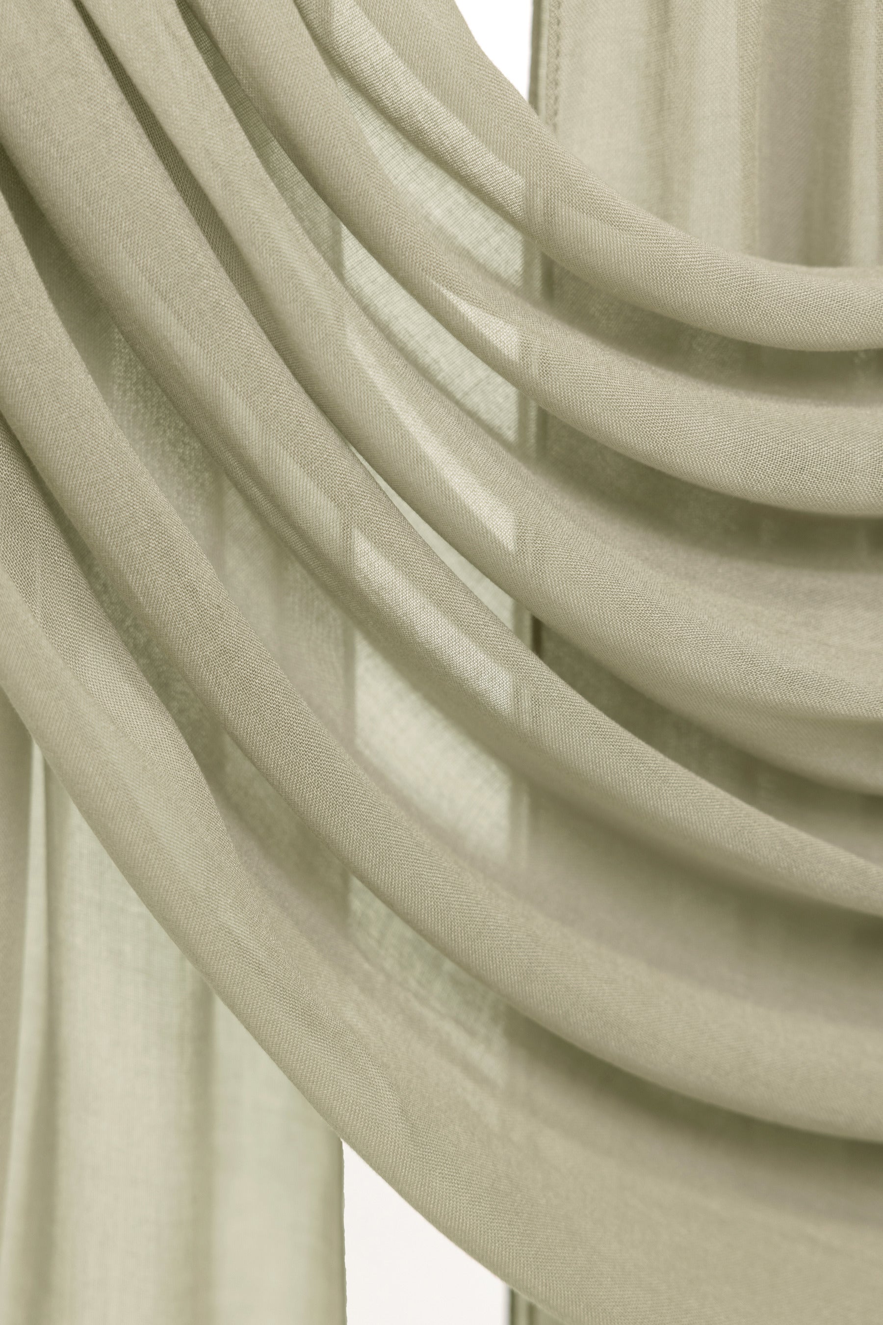 Close-up of draped sheer curtains in a light warm beige or cream tone, showing soft folds and translucent fabric texture.