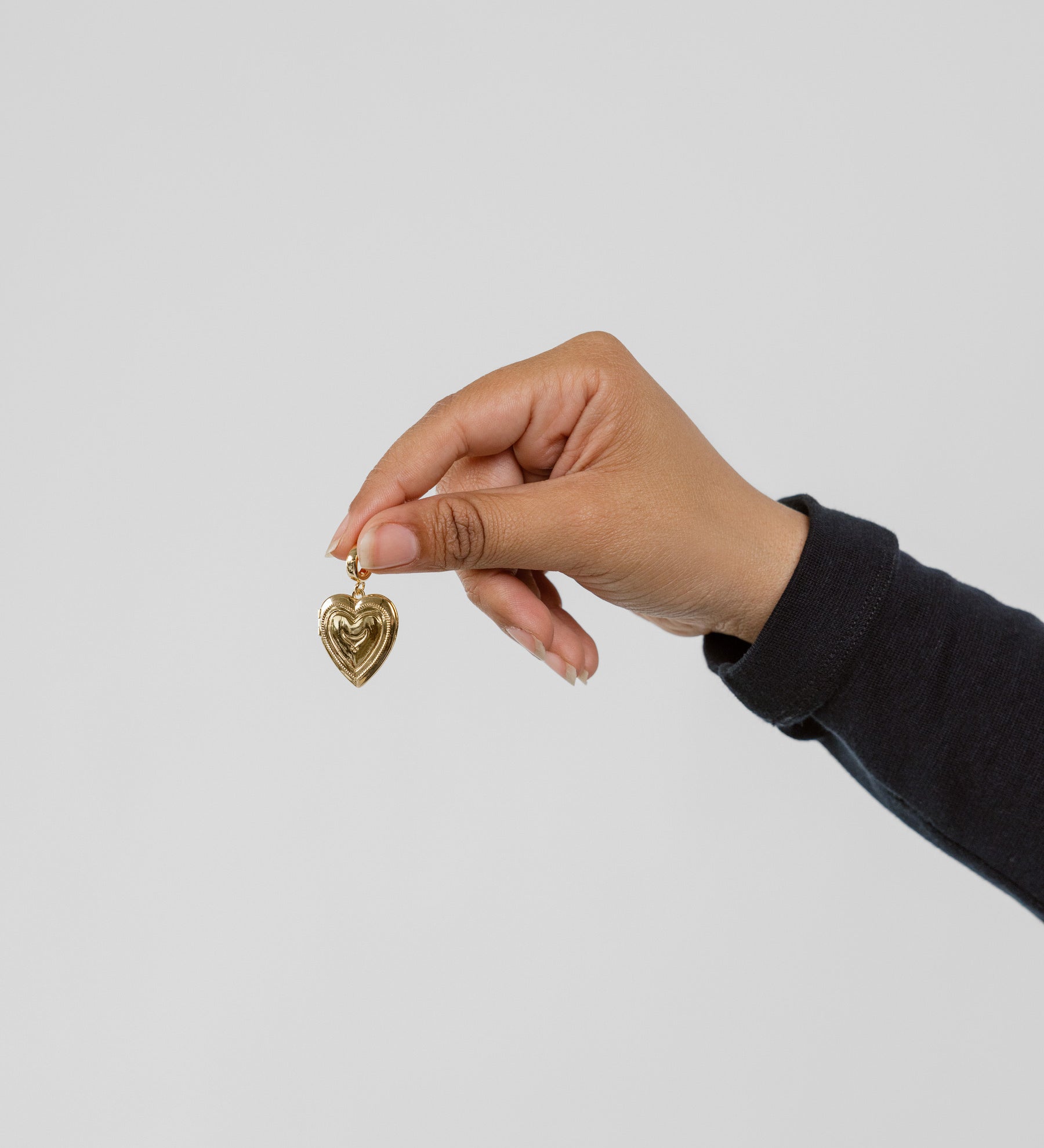 Hand holding a gold heart-shaped pendant against a plain background