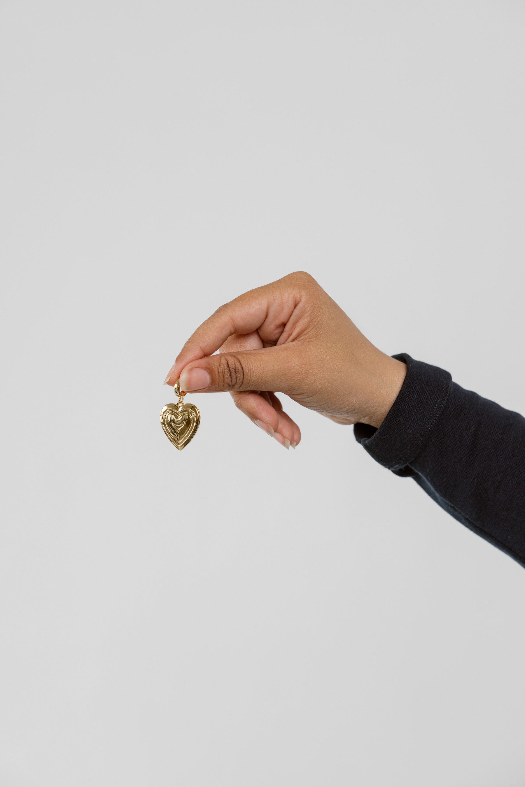 Hand holding a gold heart-shaped pendant against a plain background