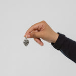 Hand holding a silver heart-shaped pendant against a plain background