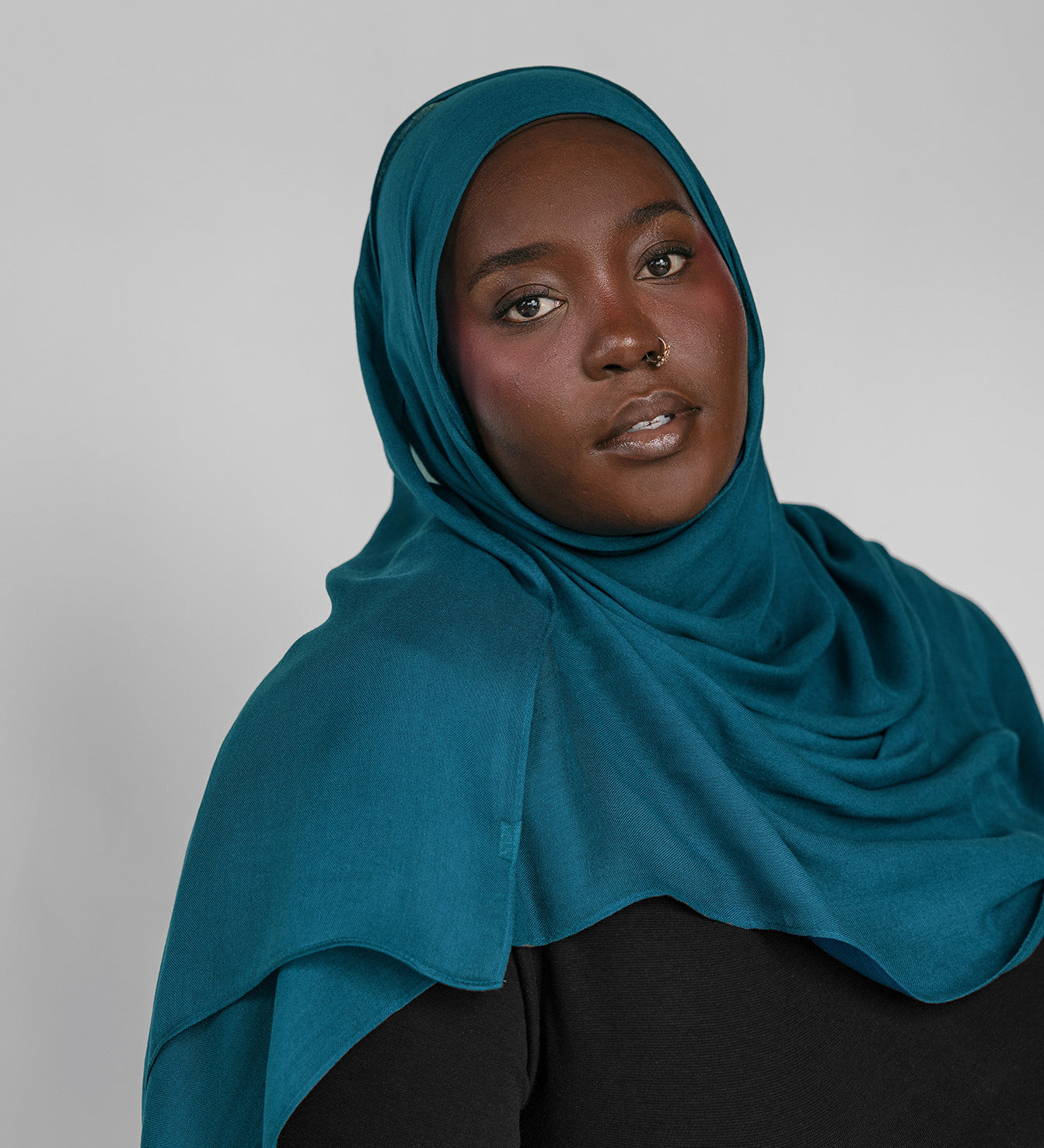 Woman wearing a teal hijab against a plain background