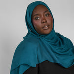 Woman wearing a teal hijab against a plain background