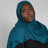 Woman wearing a teal hijab against a plain background