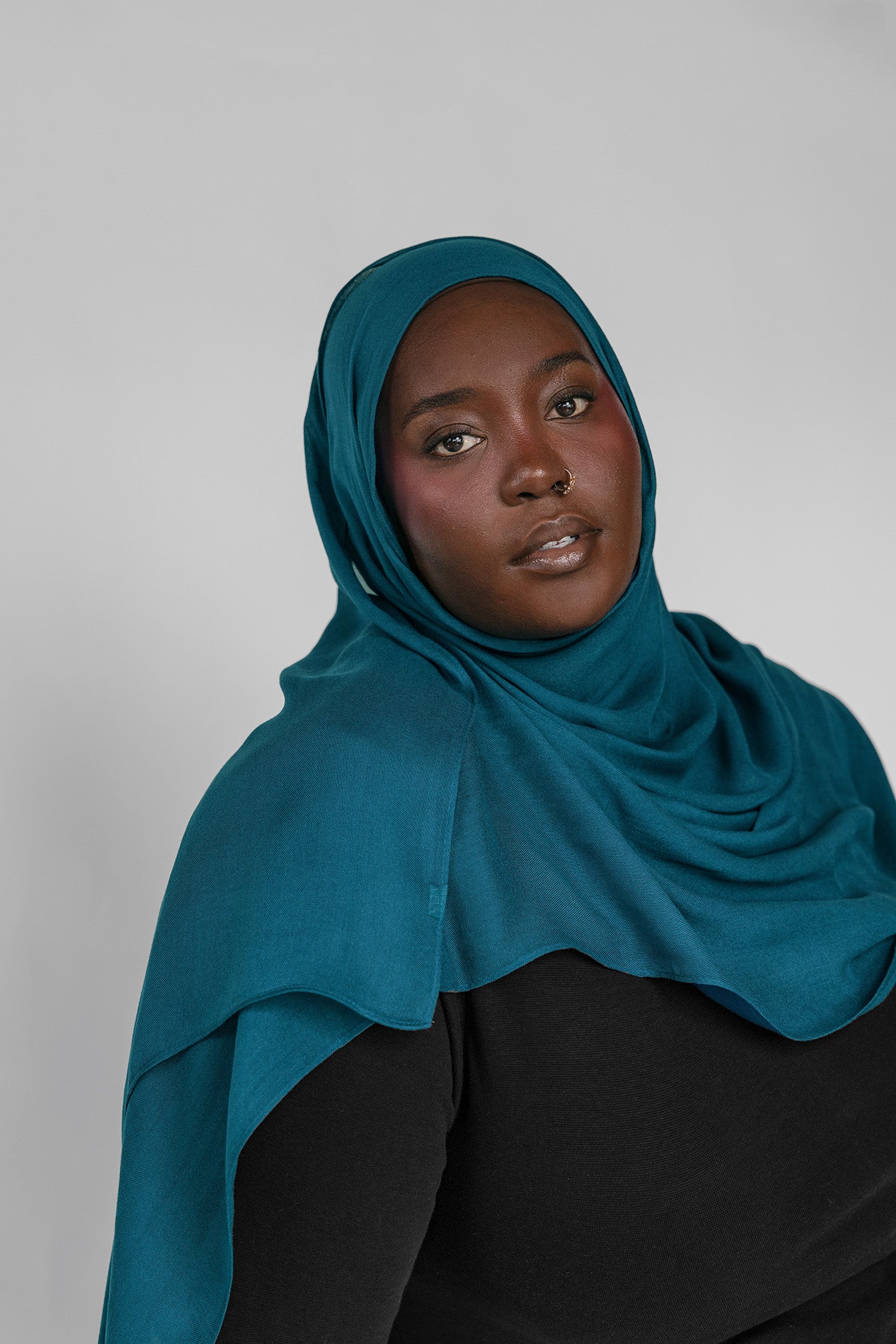 Woman wearing a teal hijab against a plain background