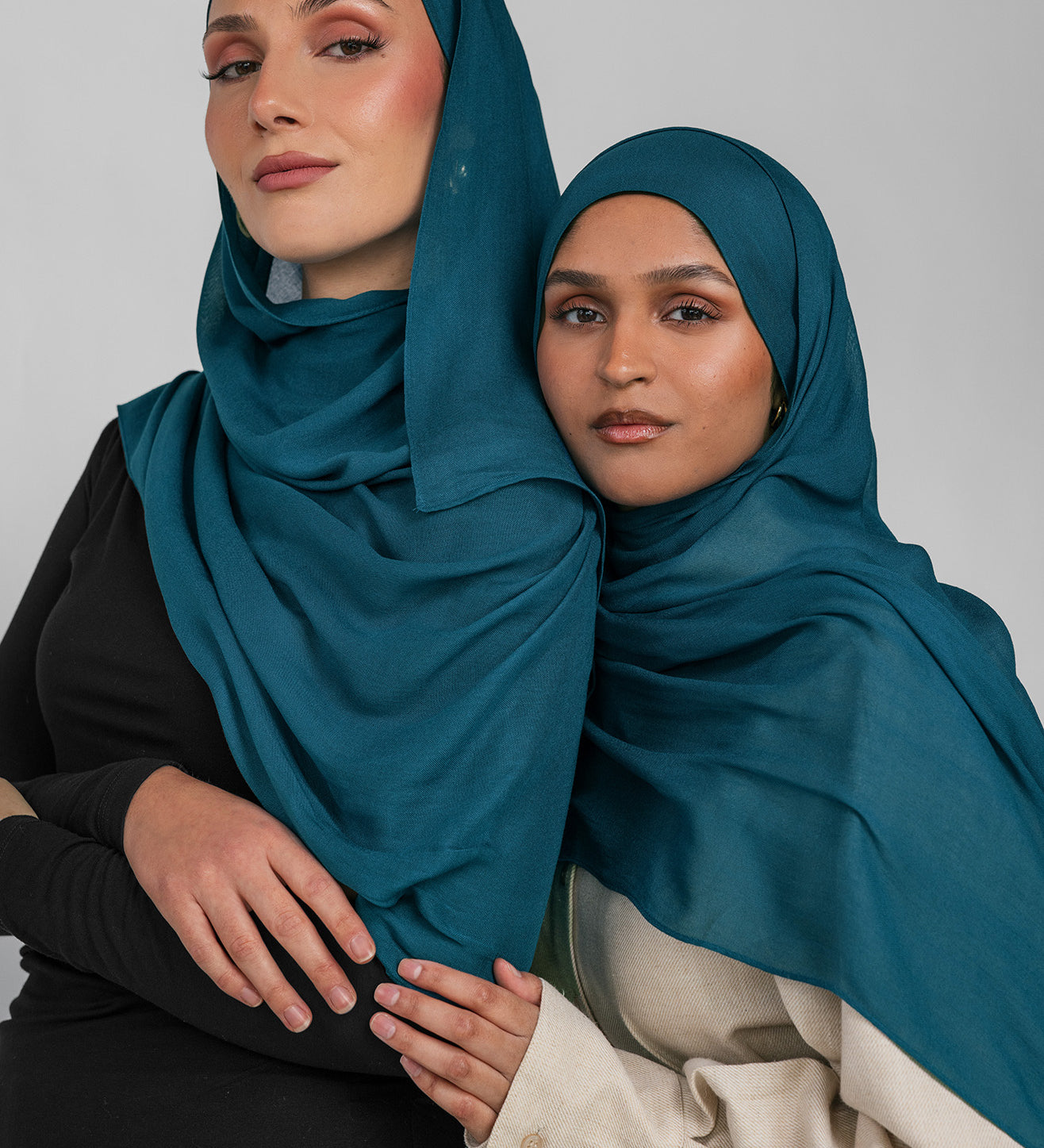 Two women wearing teal hijabs against a plain background
