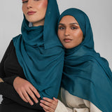 Two women wearing teal hijabs against a plain background
