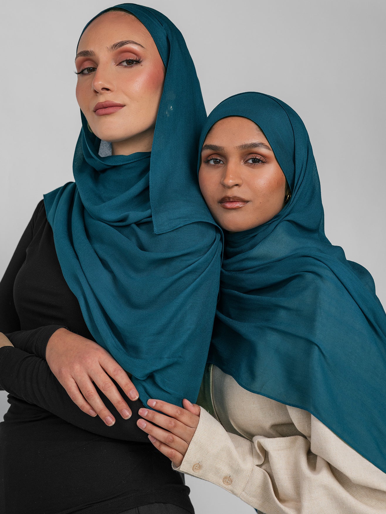 Two women wearing teal hijabs against a plain background