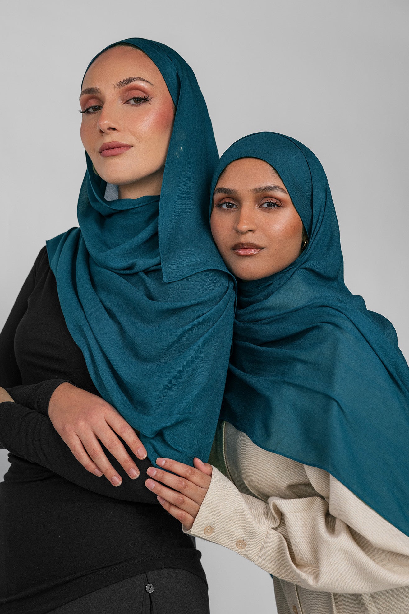 Two women wearing teal hijabs against a plain background