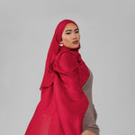 Woman wearing a red hijab and brown outfit on a gray background