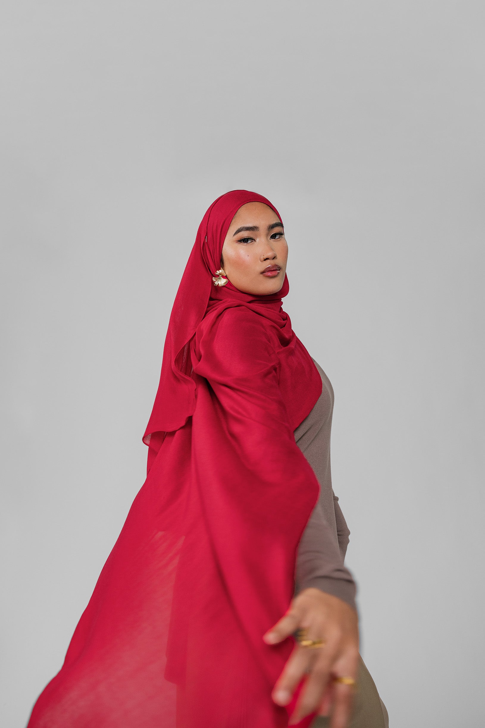 Woman wearing a red hijab and brown outfit on a gray background