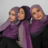 Three women wearing purple ombre hijabs sitting side by side against a plain background