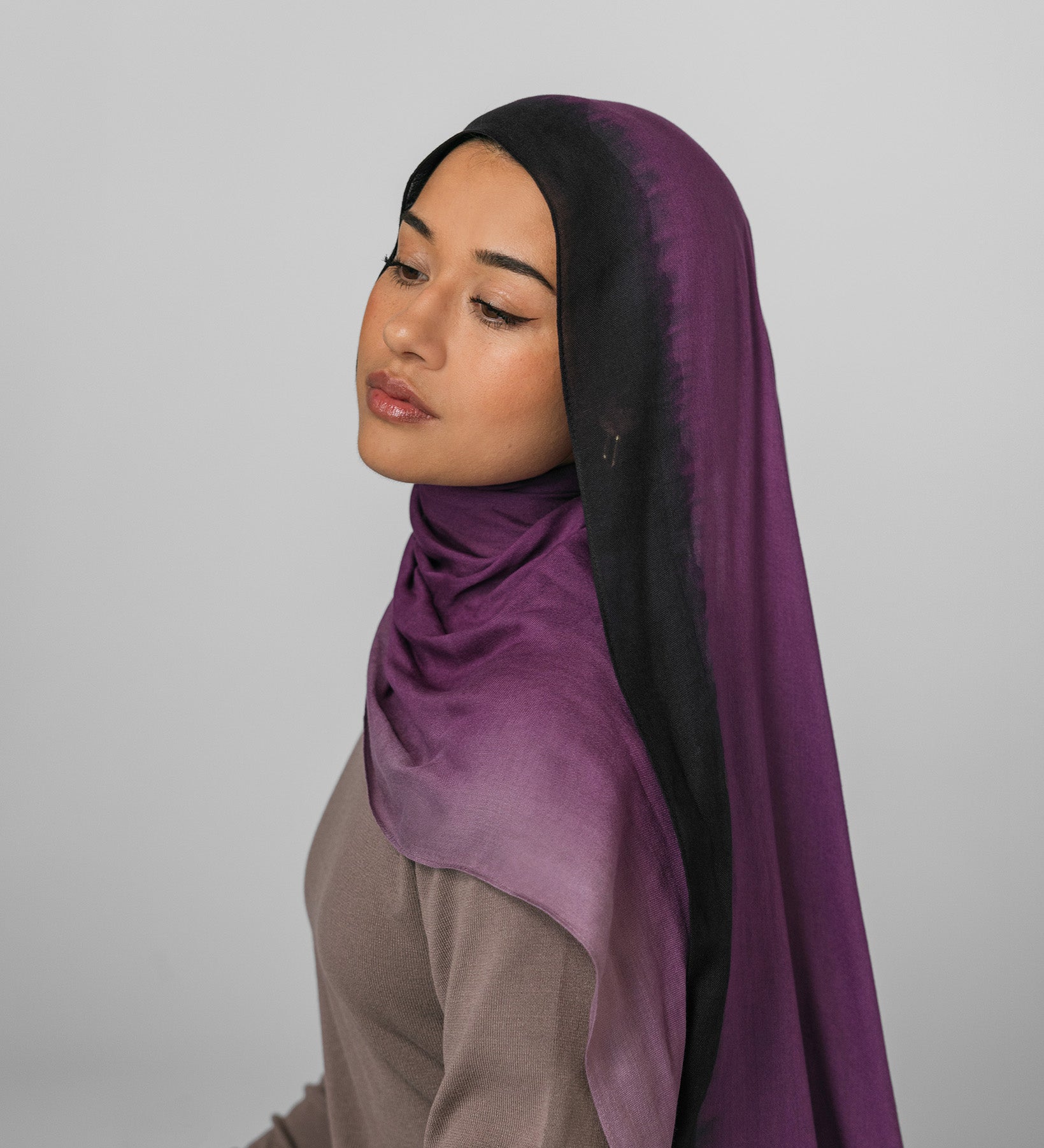 Woman wearing a purple ombre hijab against a plain background