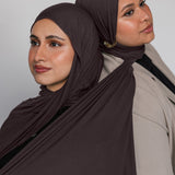 Two women wearing brown hijabs against a plain background
