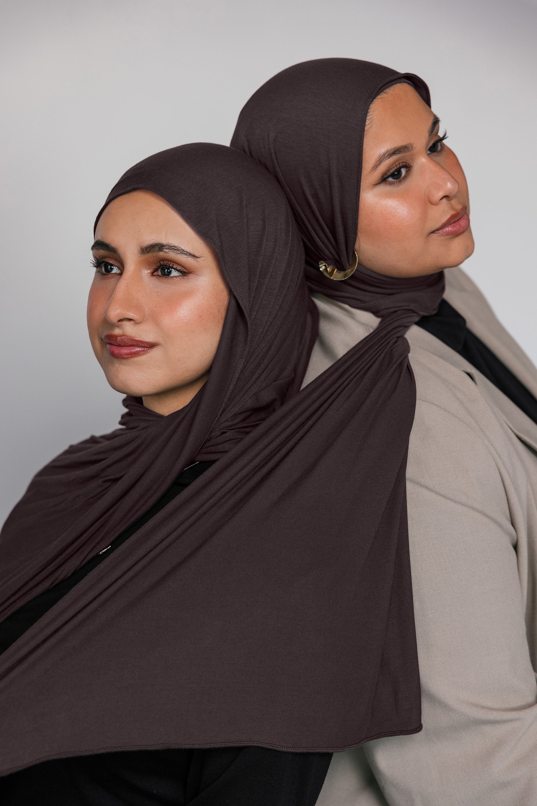 Two women wearing brown hijabs against a plain background