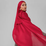 Woman wearing a red hijab against a gray background