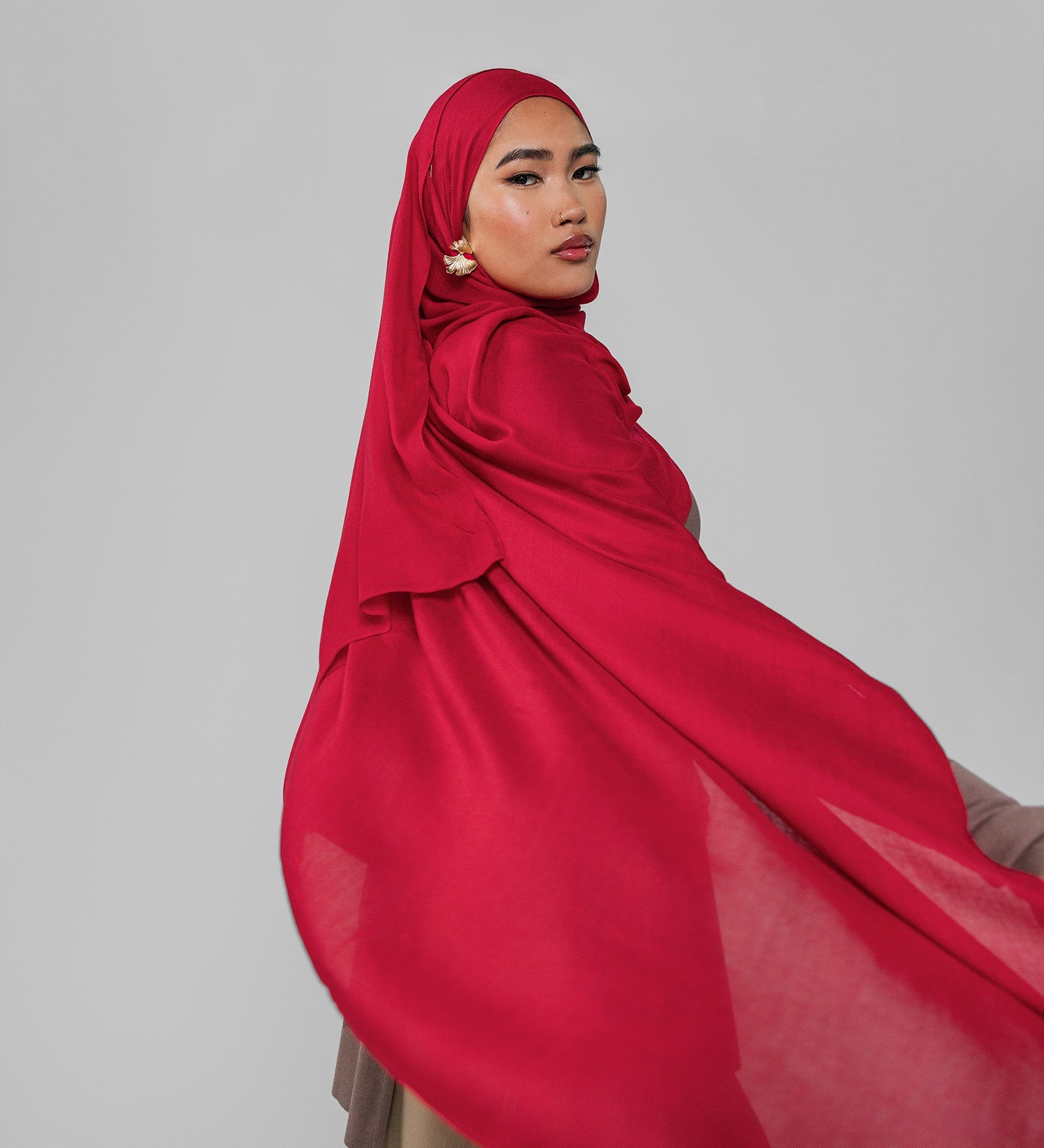 Woman wearing a red hijab against a gray background