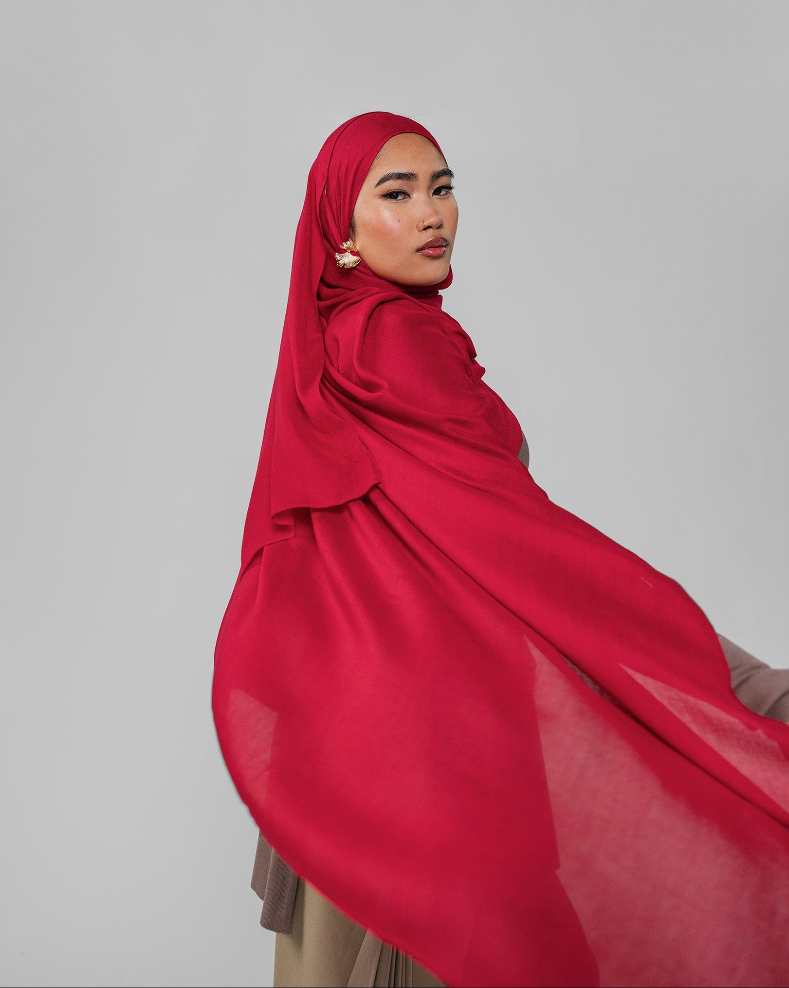 Woman wearing a red hijab against a gray background