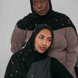 Two women wearing black hijabs with star patterns on a gray background